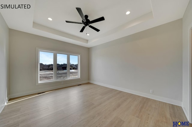 empty room with light wood-style flooring, baseboards, and a tray ceiling