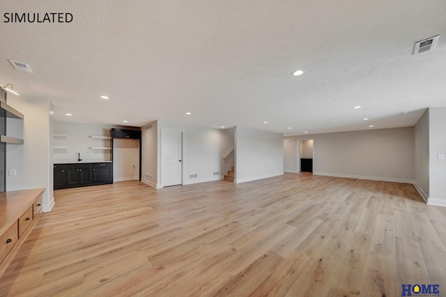 unfurnished living room with light wood finished floors, visible vents, and stairway