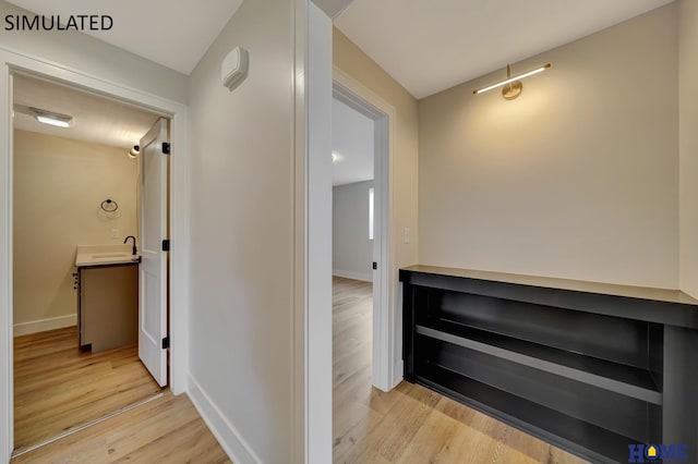 hall with a sink, baseboards, and light wood-style floors