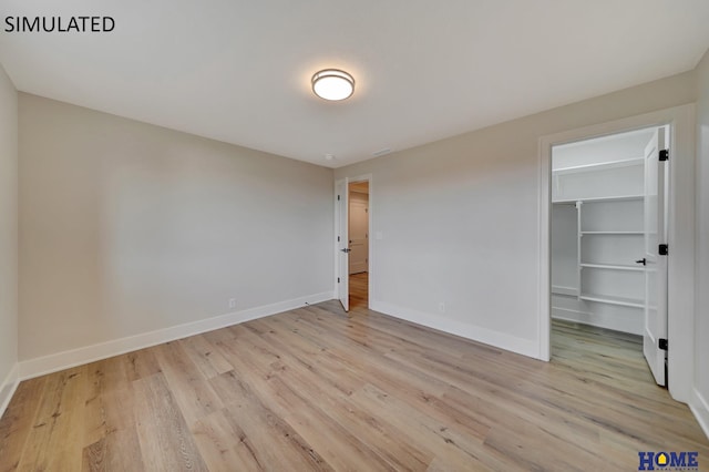 unfurnished bedroom with light wood finished floors, a closet, a walk in closet, and baseboards