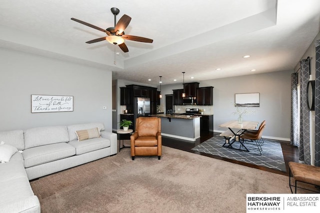 living area featuring a ceiling fan, baseboards, a tray ceiling, recessed lighting, and a fireplace