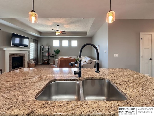 kitchen with a sink, open floor plan, a fireplace, a raised ceiling, and light stone countertops