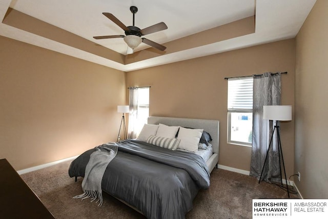 carpeted bedroom featuring baseboards, a tray ceiling, and a ceiling fan