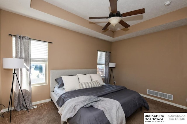 carpeted bedroom with a tray ceiling, visible vents, baseboards, and a ceiling fan