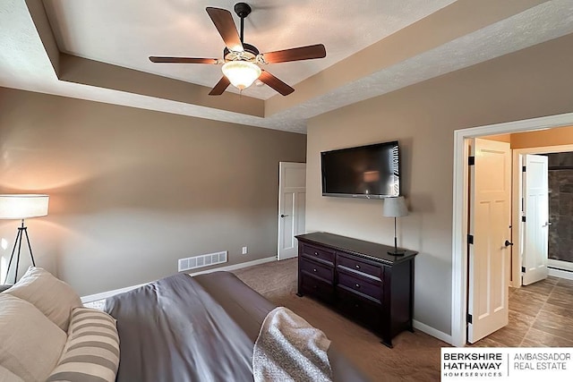 bedroom with visible vents, a textured ceiling, baseboards, and a tray ceiling