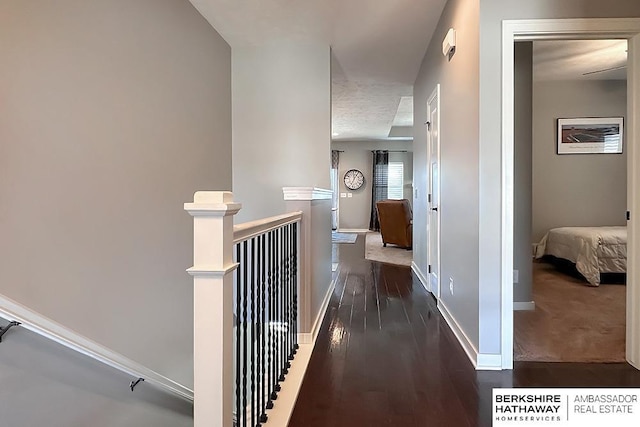 hall featuring wood finished floors, an upstairs landing, and baseboards