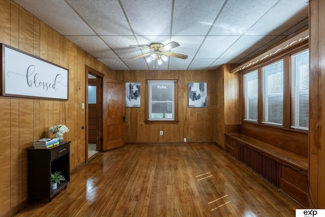 interior space featuring wood walls, a paneled ceiling, a ceiling fan, and wood finished floors