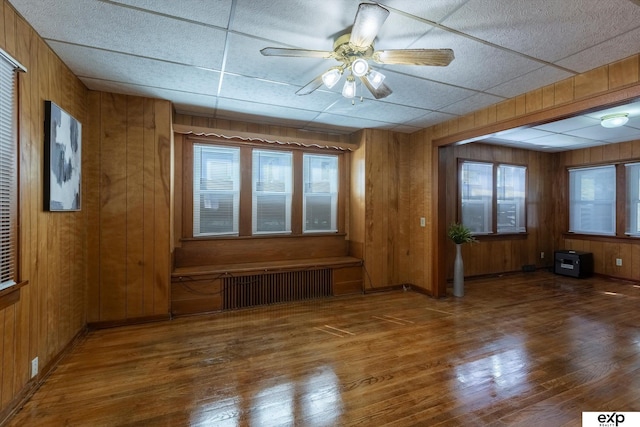 unfurnished room featuring a ceiling fan, wooden walls, wood finished floors, and radiator heating unit