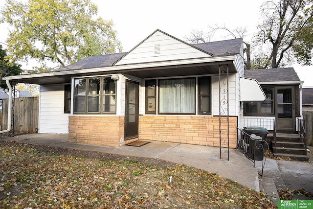 bungalow-style home featuring a sunroom, stone siding, and roof with shingles