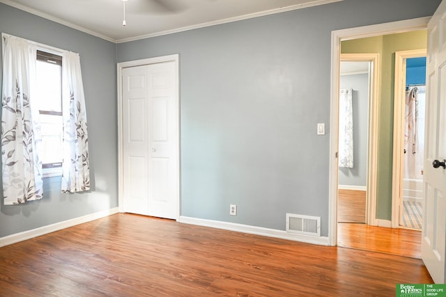 unfurnished bedroom with wood finished floors, visible vents, baseboards, ornamental molding, and a closet