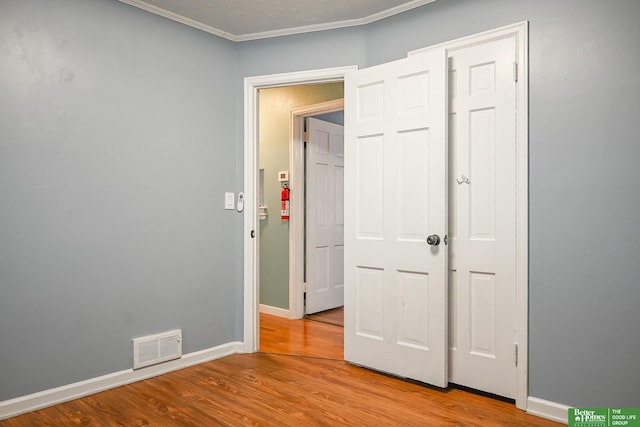 unfurnished bedroom with ornamental molding, wood finished floors, visible vents, and baseboards