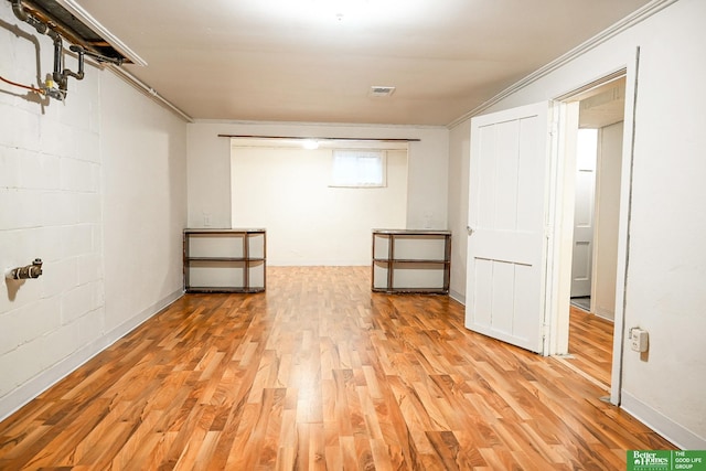 basement with crown molding, concrete block wall, light wood-style floors, and visible vents