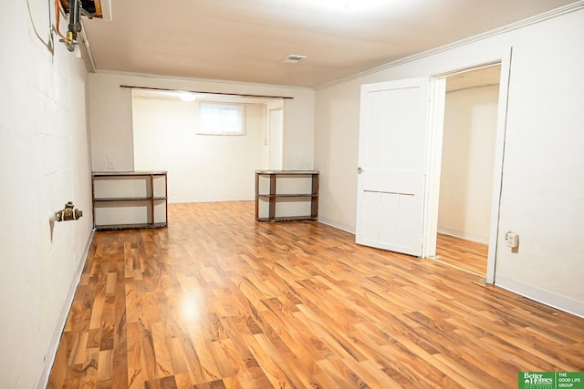 basement with visible vents, light wood-style flooring, and crown molding