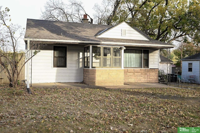 bungalow-style house with stone siding, a chimney, a patio, and a shingled roof