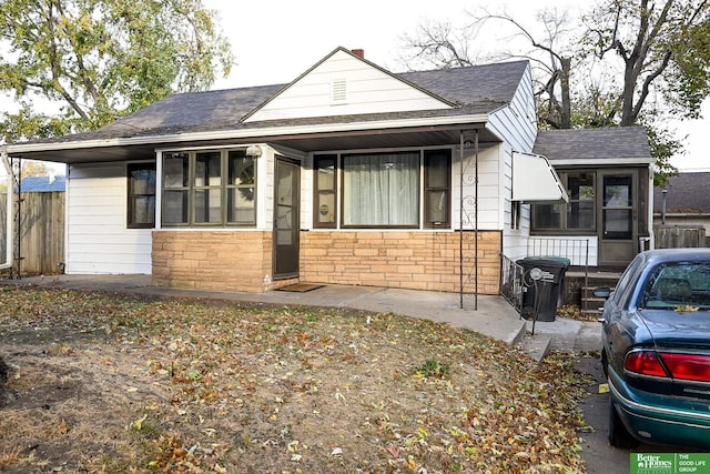 bungalow featuring stone siding, roof with shingles, and a sunroom