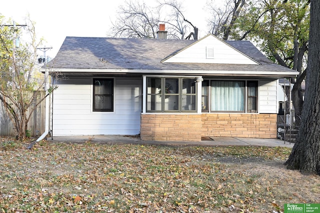 bungalow-style house featuring fence, stone siding, roof with shingles, and a chimney