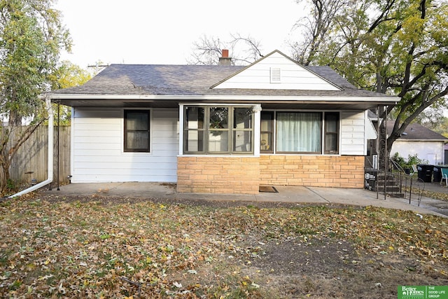 bungalow-style house with a chimney, stone siding, a shingled roof, and fence