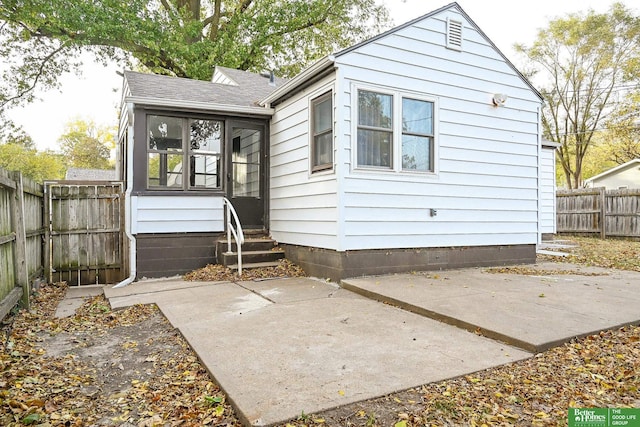 back of house featuring a patio, roof with shingles, a fenced backyard, and a sunroom