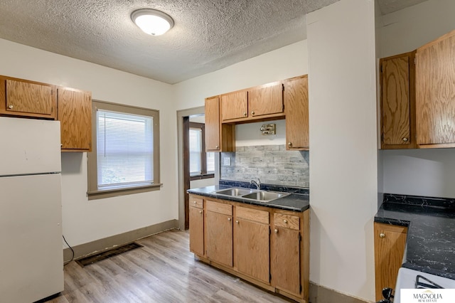 kitchen with light wood-type flooring, a sink, tasteful backsplash, dark countertops, and freestanding refrigerator