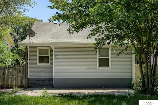 view of property exterior with a shingled roof, a patio, and fence