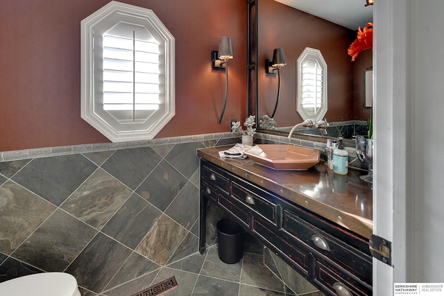 half bath featuring a wealth of natural light, toilet, tile walls, and vanity