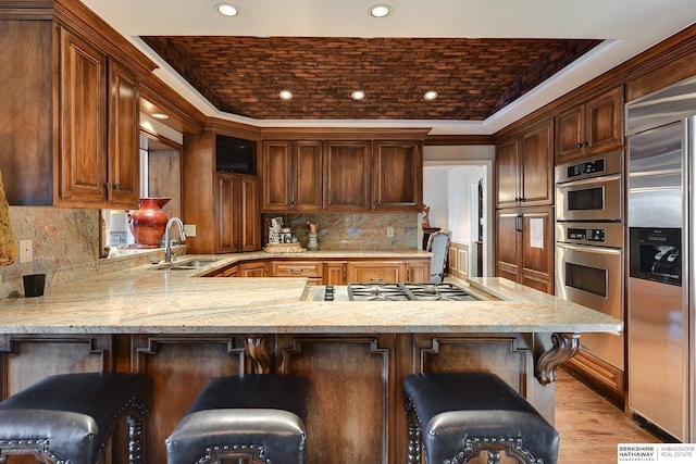 kitchen featuring a peninsula, brick ceiling, light stone countertops, and stainless steel appliances