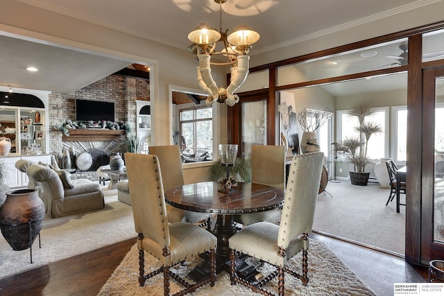 dining room with a brick fireplace, crown molding, an inviting chandelier, and wood finished floors