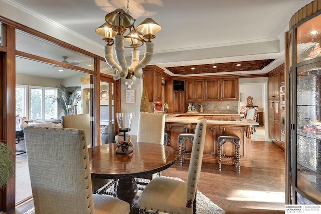 dining area with crown molding, light wood-style flooring, and ceiling fan with notable chandelier