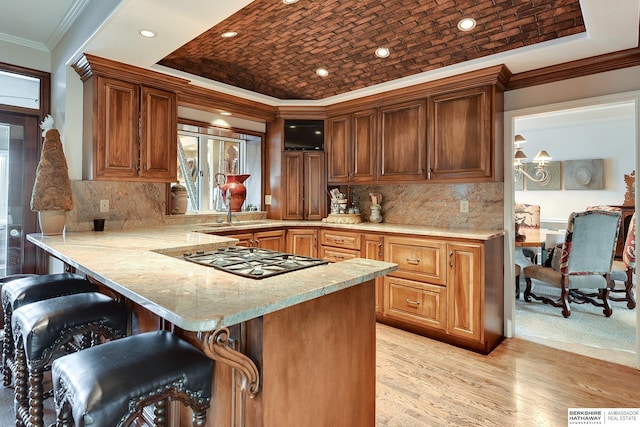 kitchen featuring ornamental molding, a kitchen breakfast bar, gas stovetop, a peninsula, and light wood finished floors