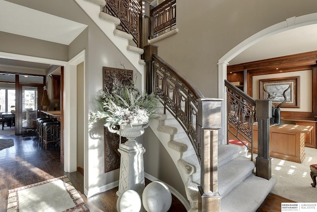 stairway with wood finished floors, baseboards, and a towering ceiling