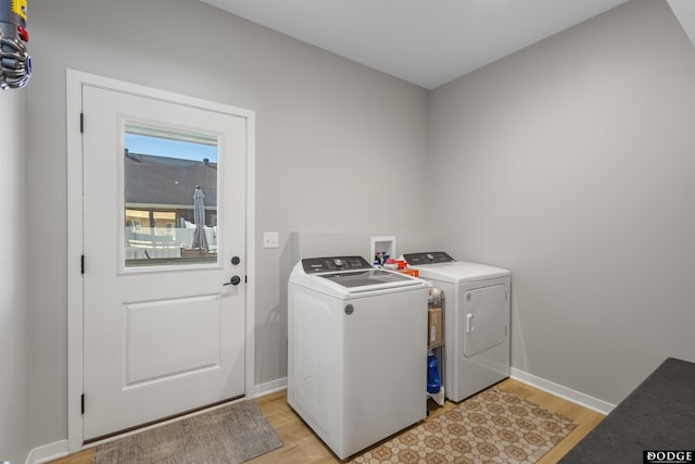 clothes washing area featuring washing machine and clothes dryer, laundry area, baseboards, and light wood-style floors