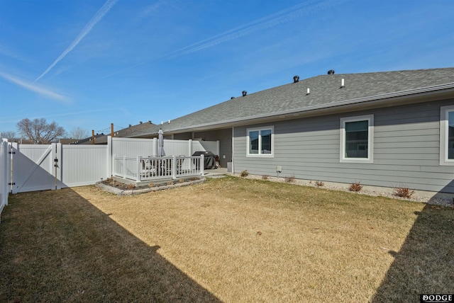 back of house with a shingled roof, fence, a yard, and a gate