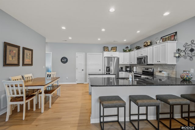 kitchen featuring tasteful backsplash, stainless steel appliances, light wood-style floors, a peninsula, and white cabinets