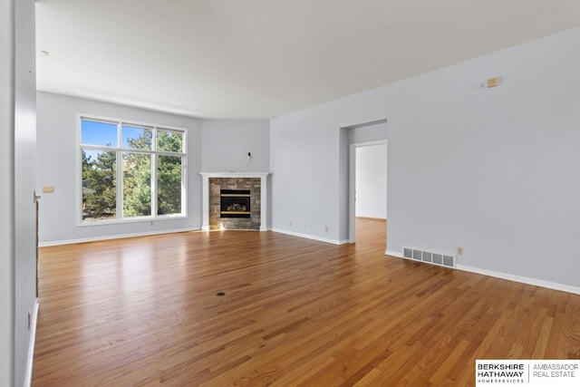 unfurnished living room featuring baseboards, visible vents, a stone fireplace, and light wood-style floors