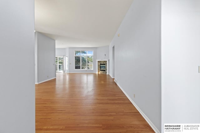 unfurnished living room with baseboards, a glass covered fireplace, and light wood finished floors