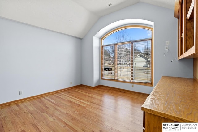 unfurnished dining area featuring baseboards, lofted ceiling, and light wood-style floors