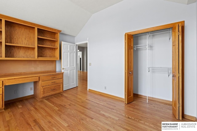 unfurnished office featuring built in desk, baseboards, light wood-style floors, and vaulted ceiling