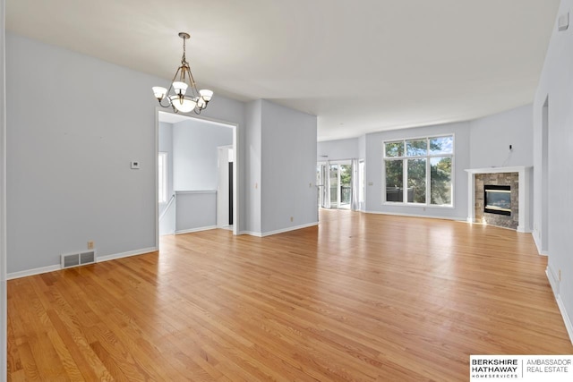 unfurnished living room with visible vents, baseboards, a chandelier, light wood-style flooring, and a tile fireplace