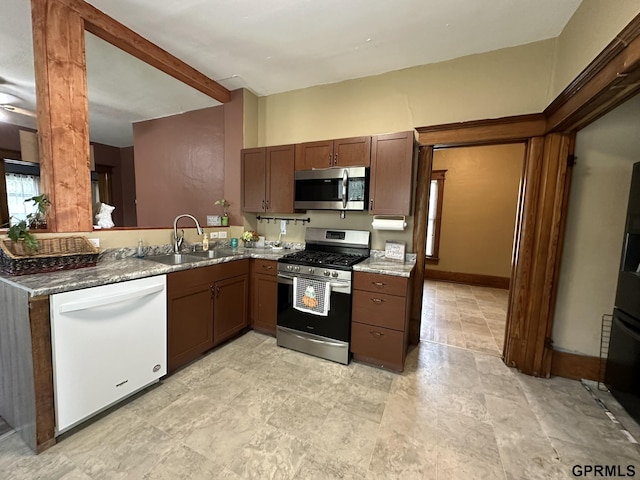 kitchen featuring baseboards, beam ceiling, stone countertops, a sink, and stainless steel appliances