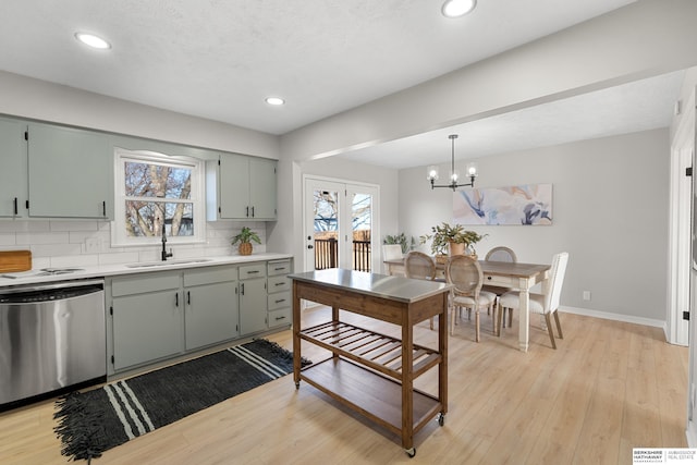 kitchen with a sink, stainless steel dishwasher, light wood finished floors, decorative backsplash, and baseboards