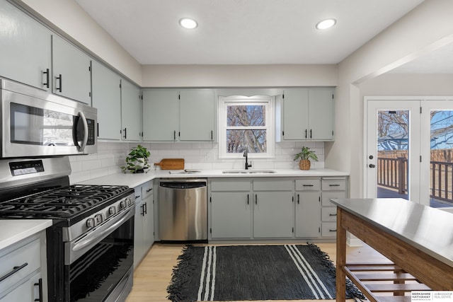 kitchen featuring light wood-style flooring, gray cabinetry, decorative backsplash, a sink, and appliances with stainless steel finishes