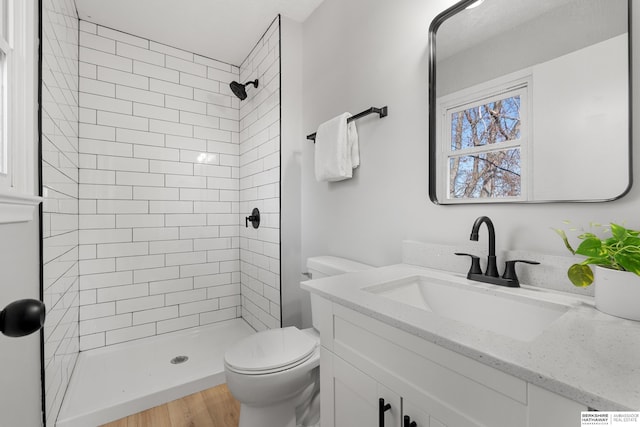 bathroom featuring toilet, wood finished floors, vanity, and a tile shower