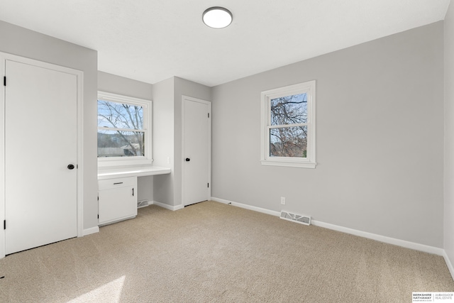 unfurnished bedroom featuring visible vents, light carpet, baseboards, and built in desk