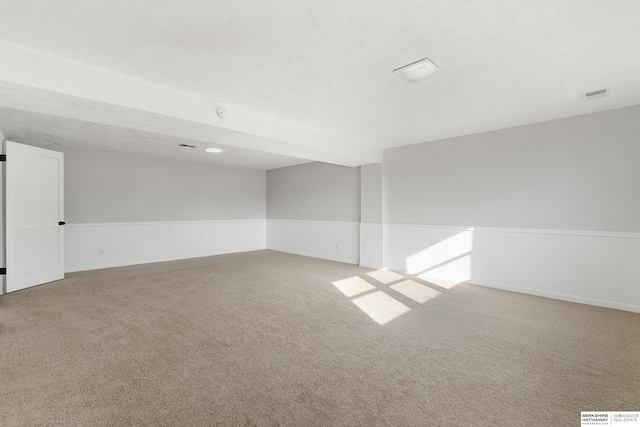 carpeted spare room with visible vents, a wainscoted wall, and a textured ceiling