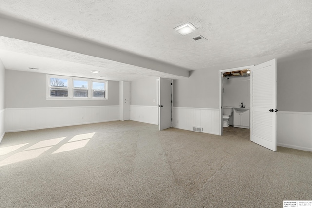 interior space featuring visible vents, a wainscoted wall, carpet flooring, a textured ceiling, and a sink