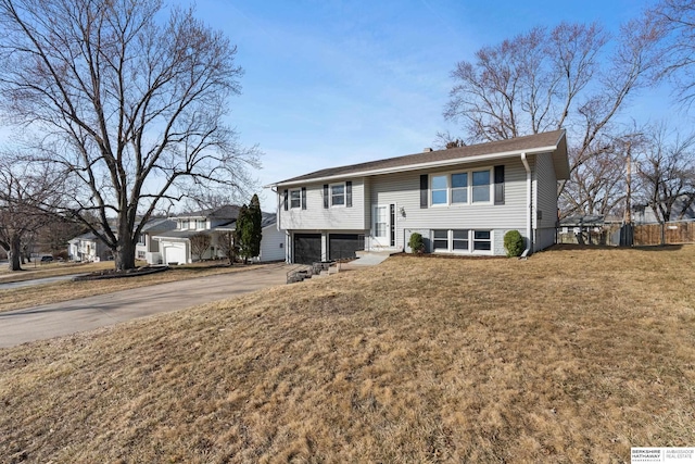 bi-level home with a garage, driveway, a front lawn, and fence