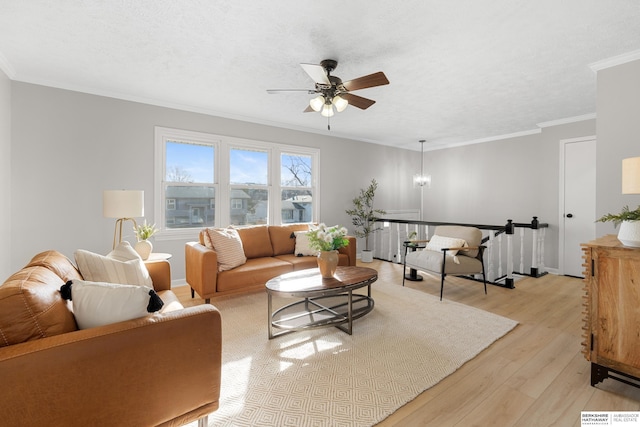 living room featuring baseboards, a textured ceiling, crown molding, ceiling fan with notable chandelier, and light wood-type flooring