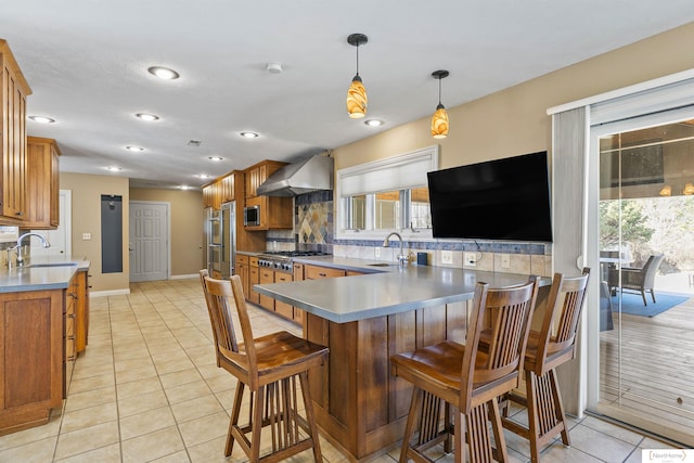 kitchen with brown cabinetry, stainless steel appliances, wall chimney exhaust hood, and a sink