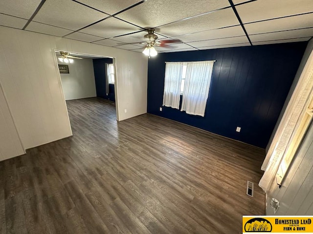 empty room with ceiling fan, visible vents, a drop ceiling, and dark wood finished floors