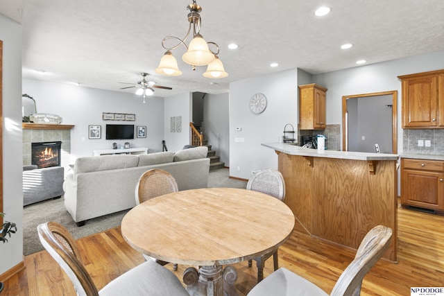 dining area featuring ceiling fan, a tiled fireplace, light wood-type flooring, stairs, and recessed lighting